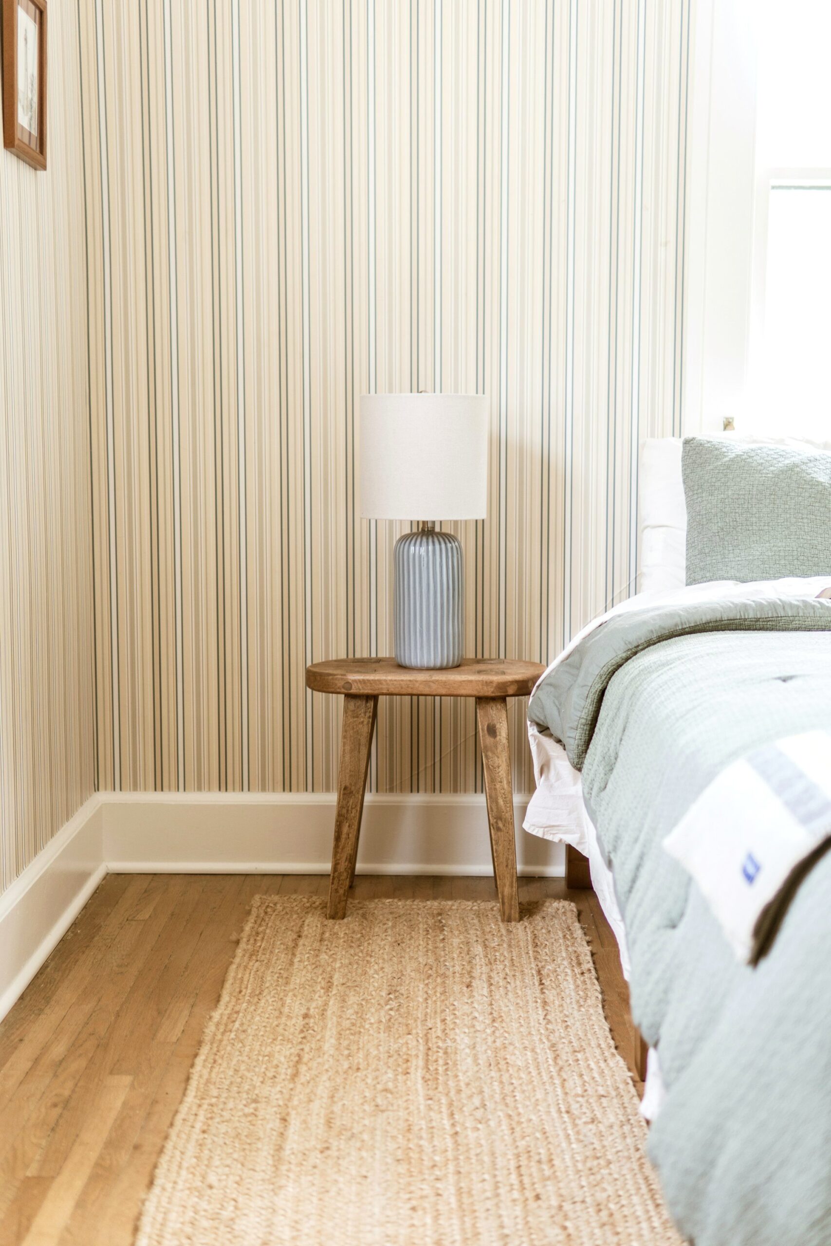 Coastal bedroom corner with jute rug, striped wallpaper and wooden side table