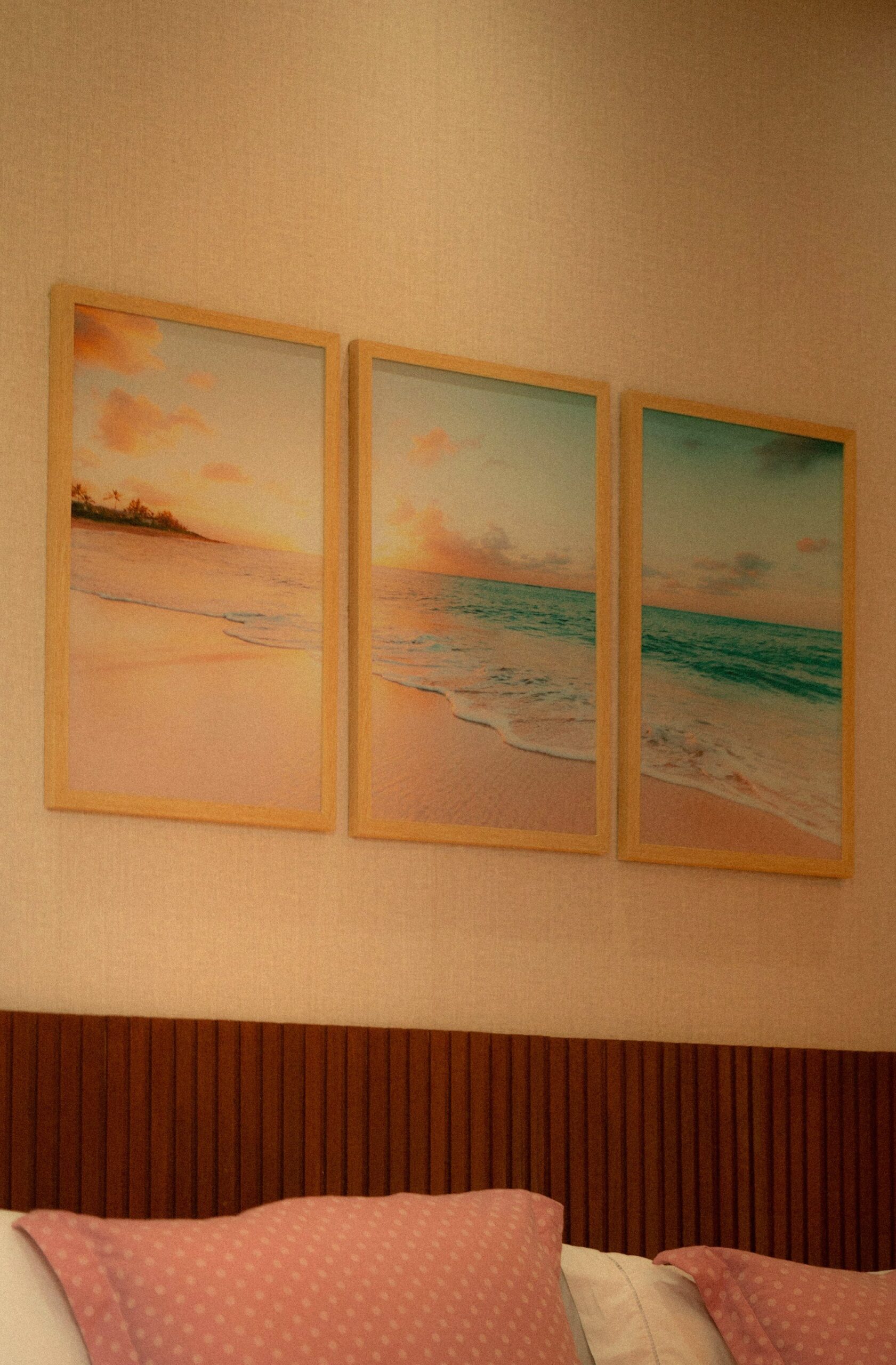Three framed beach sunset prints above a bed headboard