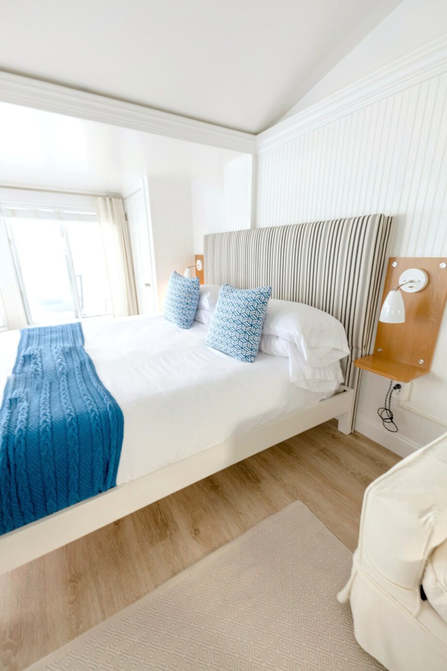 Bright coastal bedroom with white bedding, blue throw and upholstered headboard