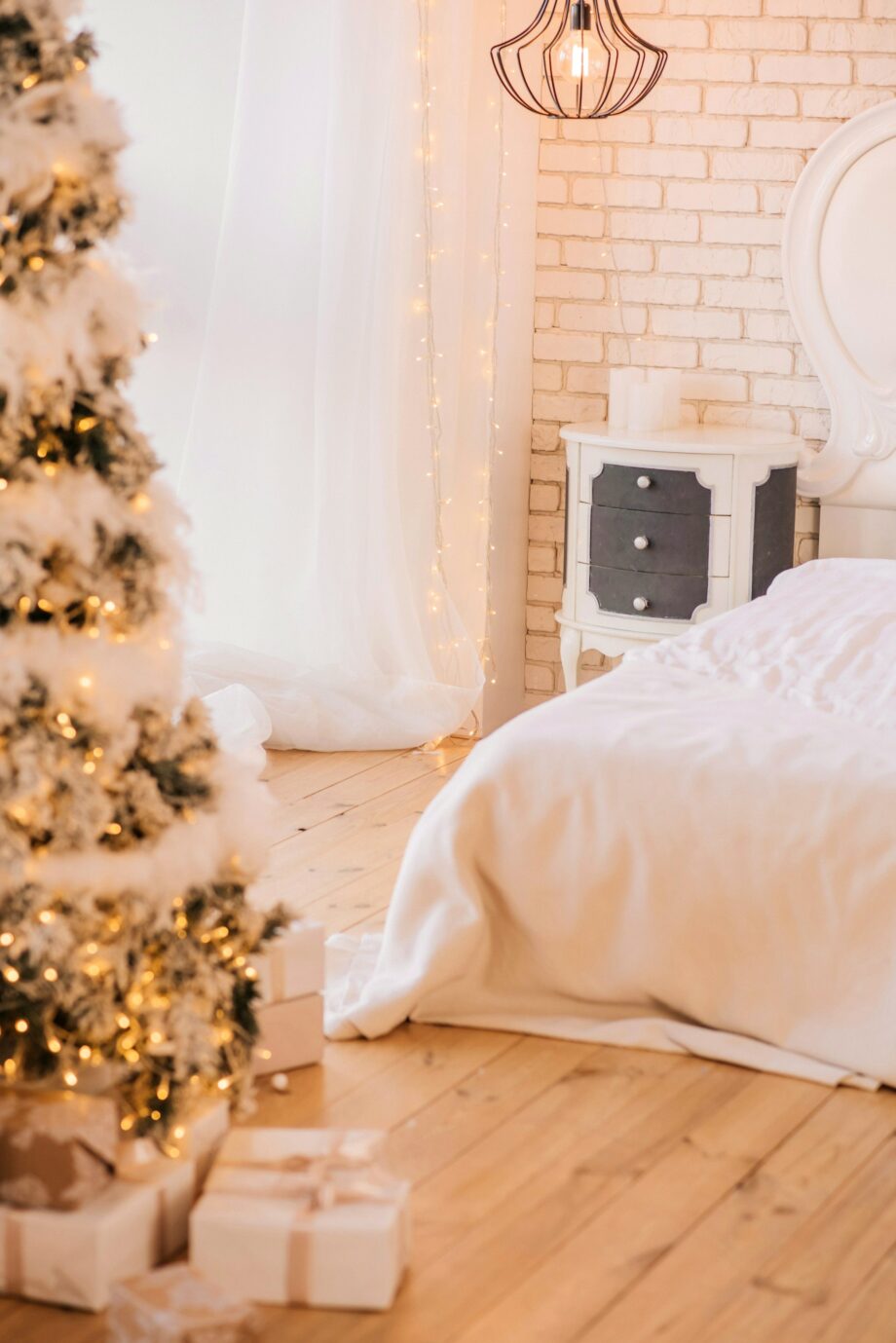 Cozy white bedroom with a lit Christmas tree and wooden floor